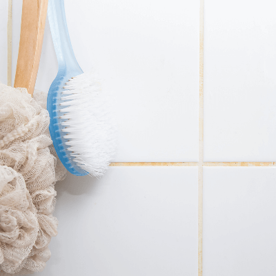 Close-up of loofah and body brush hanging on tiled wall in home bathroom